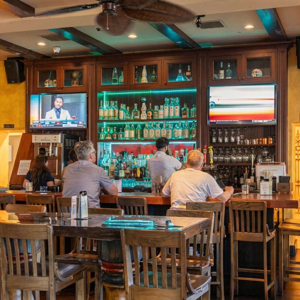 Patrons seated at a lively bar with a well-stocked liquor display and TVs in a restaurant.