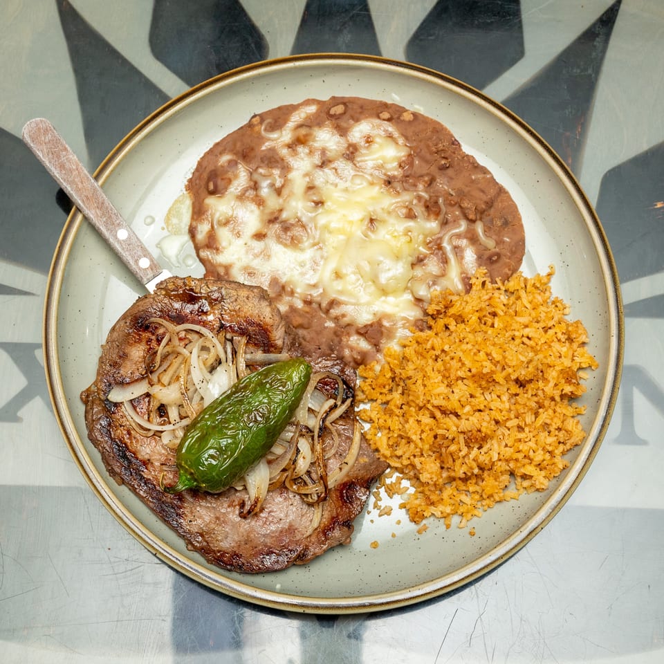 Plate featuring grilled steak with onions and green pepper, cheesy refried beans, and orange Mexican rice.