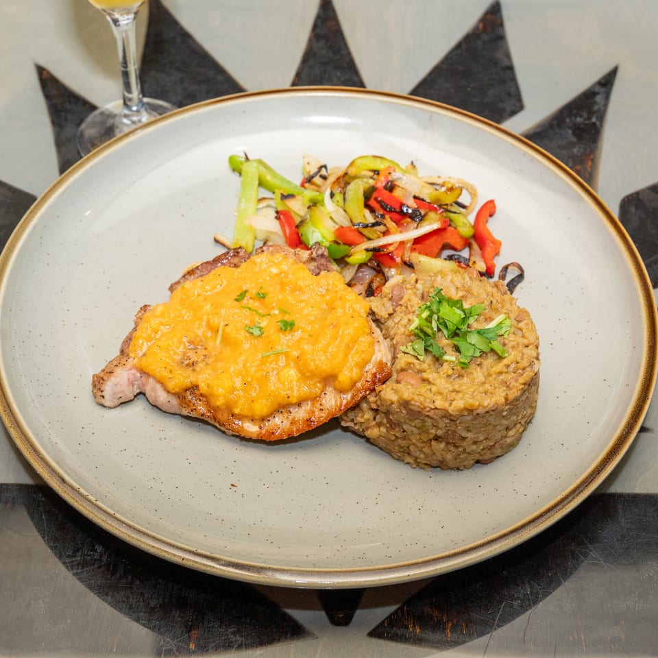 Grilled steak topped with creamy orange sauce, served with lentil patties and charred peppers on a ceramic plate.