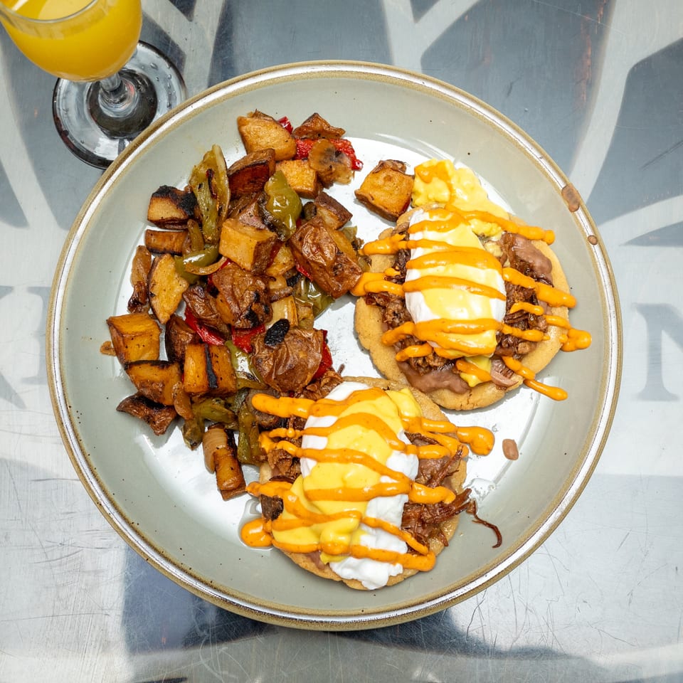 Plate of roasted potatoes and peppers with two open-faced dishes topped with melted cheese, sour cream, and orange sauce, beside orange juice.