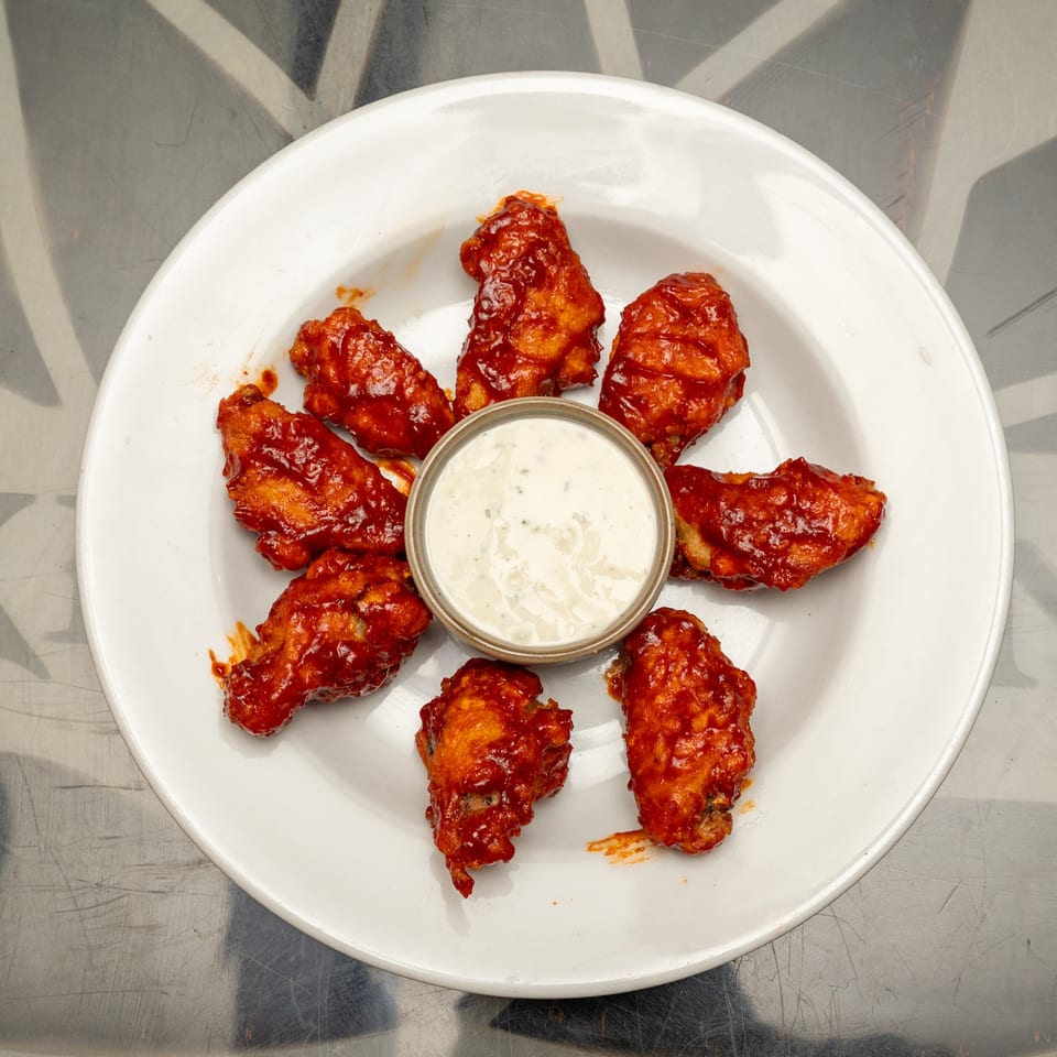 Buffalo-style chicken wings arranged around a cup of creamy dipping sauce on a white plate.